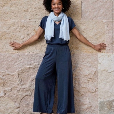 Mulher com roupa azul escura e cachecol azul claro junto a parede de pedra clara