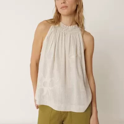 Mulher com blusa bege clara com gola alta e calças verdes.