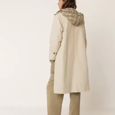 Mulher de costas a usar casaco comprido bege com capuz xadrez e calças largas castanhas.