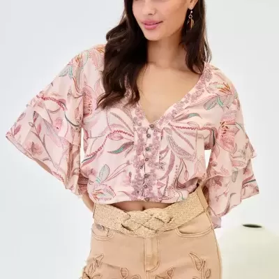 Blusa feminina rosa com padrão floral, botões e mangas amplas, calças bege bordadas e cinto trançado