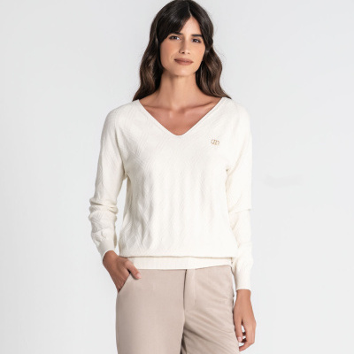 Camisola branca com padrão losangos e logo dourado, calças bege