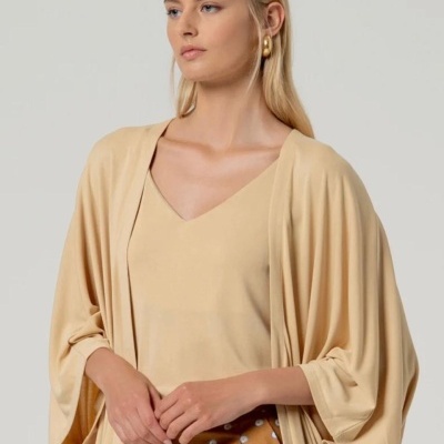 Mulher loira com camisola creme e casaco largo da mesma cor, saia castanha com flores brancas