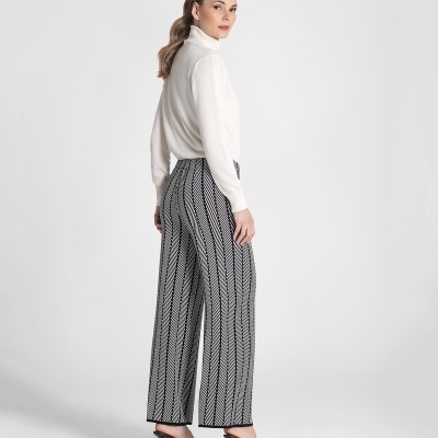 Mulher vestindo camisola branca e calças largas pretas e brancas com padrão geométrico