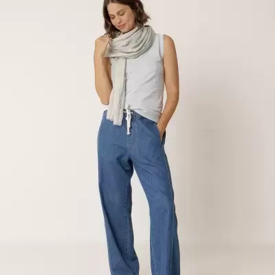 Mulher com calças de ganga largas, camisola cinza clara e lenço claro com padrão subtil.