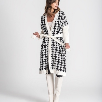 Cardigã comprido pied-de-poule preto e branco com cinto branco e botas brancas em modelo feminino