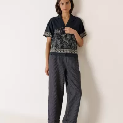 Mulher com camisa azul escura com padrão floral bege, calças cinzentas riscas finas e sandálias cinzentas