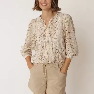 Mulher com blusa padrão geométrico creme e castanho e calções bege.