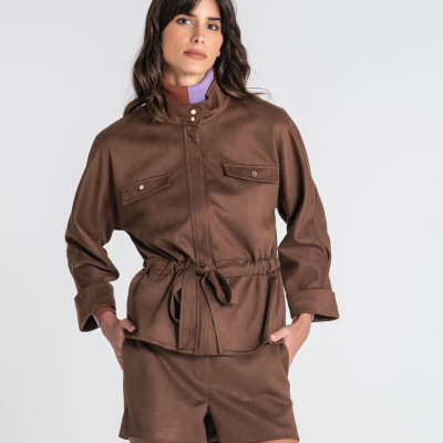 Mulher com conjunto de casaco e calções marrons com cinto ajustável e bolsos, usando camisola de gola alta castanha e lilás.