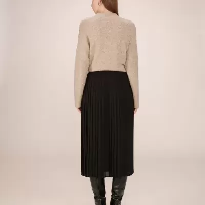 Mulher de costas com camisola bege, saia preta plissada e botas pretas