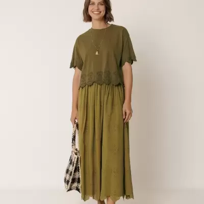 Mulher com vestido verde-oliva bordado, sandálias marrons e bolsa xadrez creme e preta