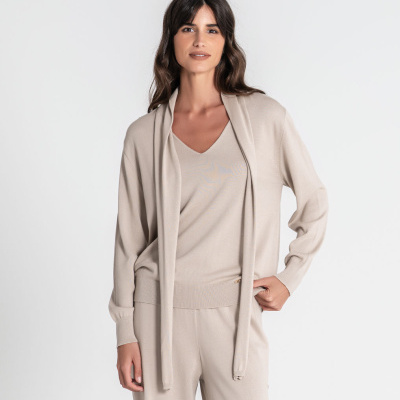 Conjunto de malha bege composto por camisola com gola cachecol, camisola de decote em V e calças largas num fundo branco.