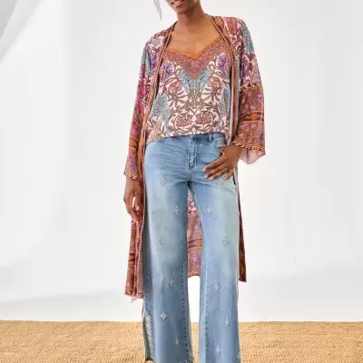 Modelo de mulher vestindo blusa e kimono estampados coloridos, calças de ganga bordadas azuis e sandálias bege