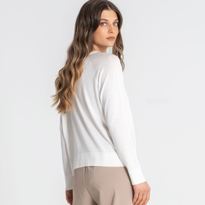 Mulher de cabelo comprido ondulado a usar camisola branca e calças bege em fundo branco