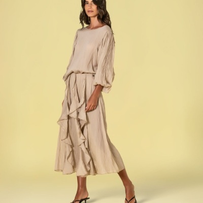 Vestido bege comprido com mangas franzidas e folhos, sandálias pretas, fundo amarelo