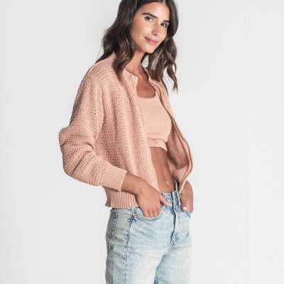 Mulher com camisola de malha rosa e calções de ganga claros em fundo branco