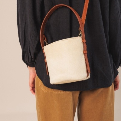 Mala pequena branca com alça castanha usada sobre roupa preta e castanha