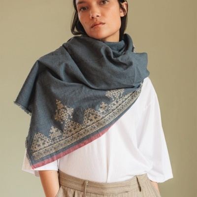 Estola azul-acinzentada bordada usada por mulher com camisa branca e calças bege