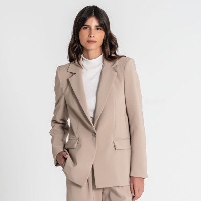 Mulher com fato bege e camisola branca em fundo branco