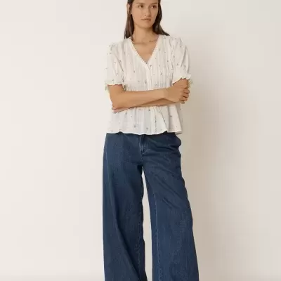 Mulher vestindo blusa branca e calças de ganga largas azuis.