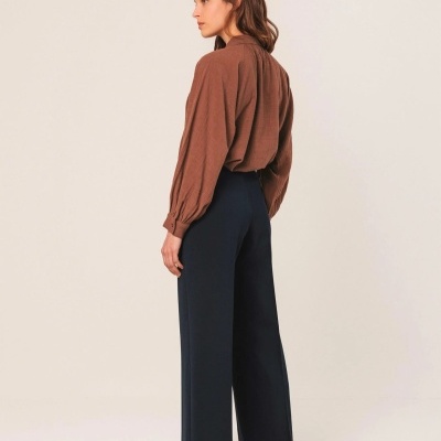 Conjunto feminino com blusa castanha e calças pretas em fundo bege