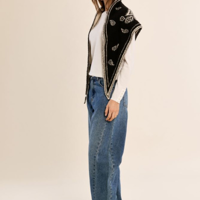 Mulher com colete preto e branco, jeans azuis largos e camisa branca