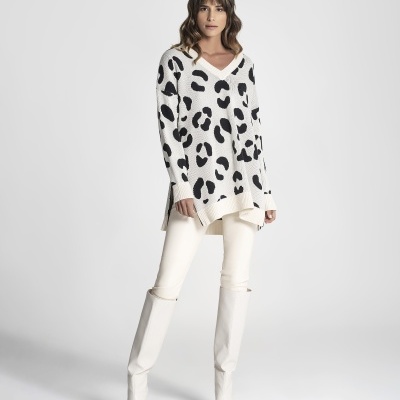 Mulher com camisola branca e padrão animal preto, calças creme e botas brancas
