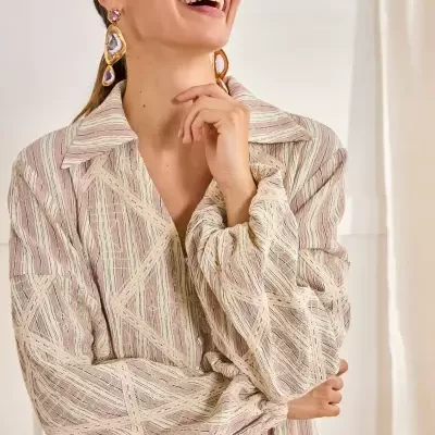 Blusa feminina listrada em tons pastel com textura em relevo e botões, usada com brincos grandes dourados e pedras rosa.