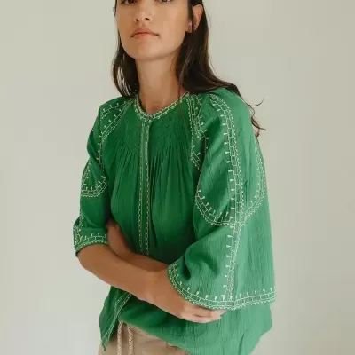 Blusa verde com bordados brancos e calções bege com cordão.