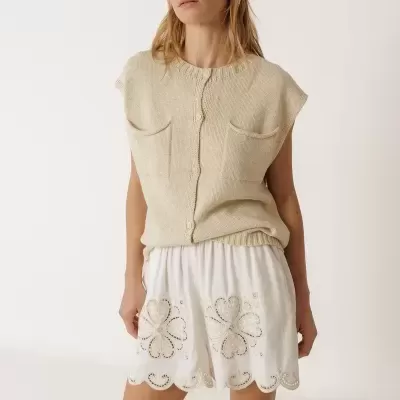 Mulher com colete bege de malha e calções brancos bordados