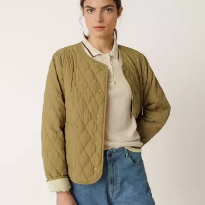 Casaco acolchoado verde-oliva com padrão de losangos, botões à frente e bolso, usado com camisa bege e jeans azul claro.