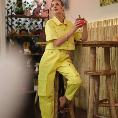 Mulher com conjunto amarelo sentada em banco alto segurando copo vermelho com palha