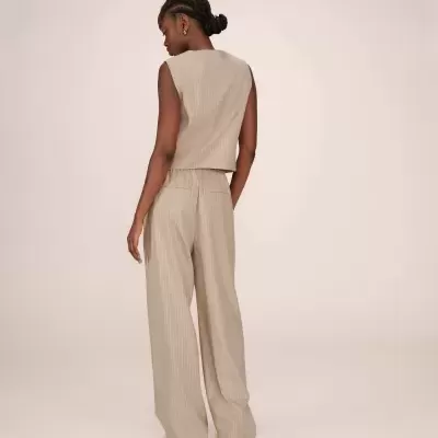 Mulher de costas a usar colete e calças largas bege com riscas finas brancas