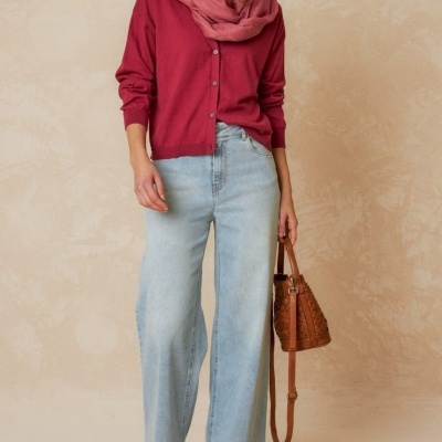 Mulher com camisola cardigan vermelha, lenço rosa, calças de ganga claras e mala castanha