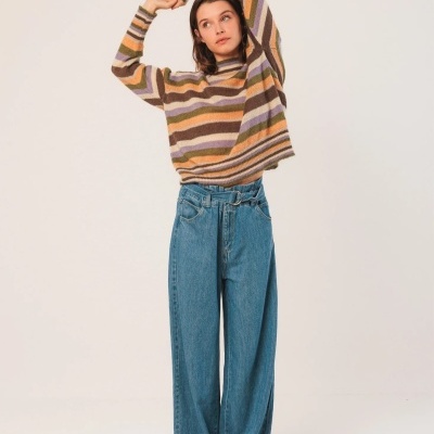 Mulher com camisola às riscas coloridas e calças de ganga largas azuis.