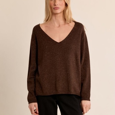 Mulher com camisola castanha brilhante e calças pretas num fundo bege.