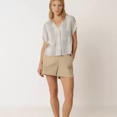 Mulher com camisa de botões e calções bege em fundo branco