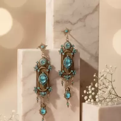 Brincos dourados com pedras azuis pendurados em blocos de mármore creme