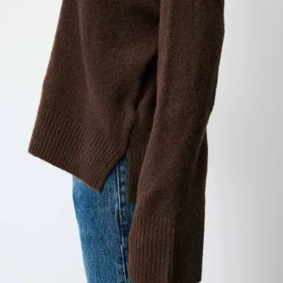 Suéter castanho de malha com calças jeans azuis em fundo branco
