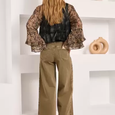 Calças largas castanhas de ganga, botas pretas, colete preto e blusa com padrão paisley castanho e preto, vista de costas.