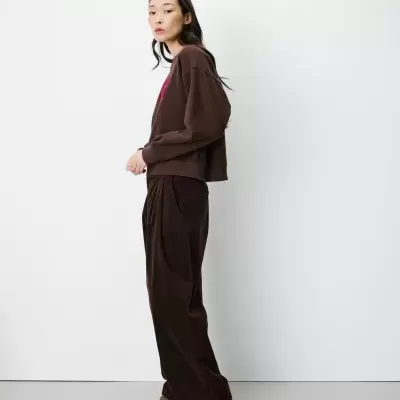 Mulher com sweatshirt castanha, calças largas de veludo castanhas e mocassins castanhos claros.