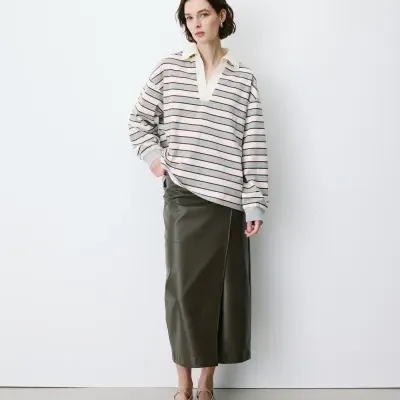 Mulher com camisola de riscas e saia midi escura em fundo branco.