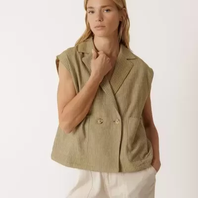 Colete feminino riscado verde com botões e calças largas bege.