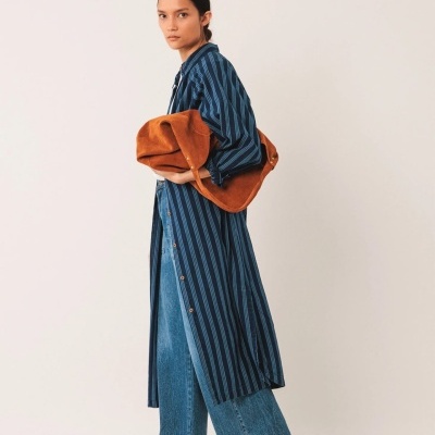 Mulher com casaco comprido azul às riscas e calças de ganga largas azuis segurando roupa castanha