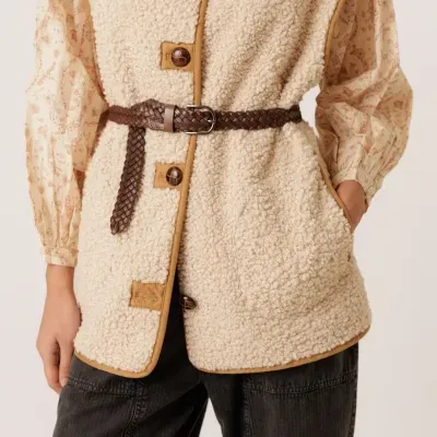 Colete creme tipo lã sherpa com botões castanhos, cinto castanho trançado, camisa creme com padrão floral castanho e calças pretas largas