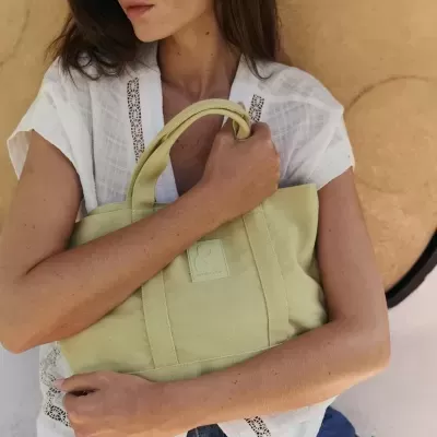 Mulher com mala de tecido verde clara e óculos escuros sentada