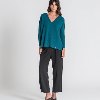 Mulher com camisola verde-azulado e calças pretas em fundo branco