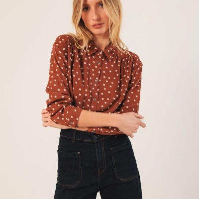 Mulher vestindo blusa castanha com bolinhas brancas e calças pretas de ganga