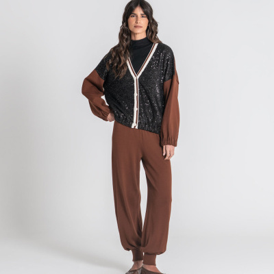 Mulher com cardigan preto de lantejoulas, blusa preta, calças castanhas e sapatilhas castanhas