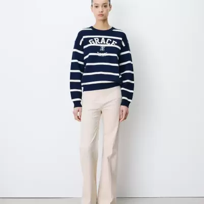 Mulher a usar camisa de malha azul com riscas brancas e calças bege against fundo branco.