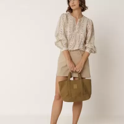 Mulher com blusa bege estampada, calções bege, sandálias e mala verde-oliva